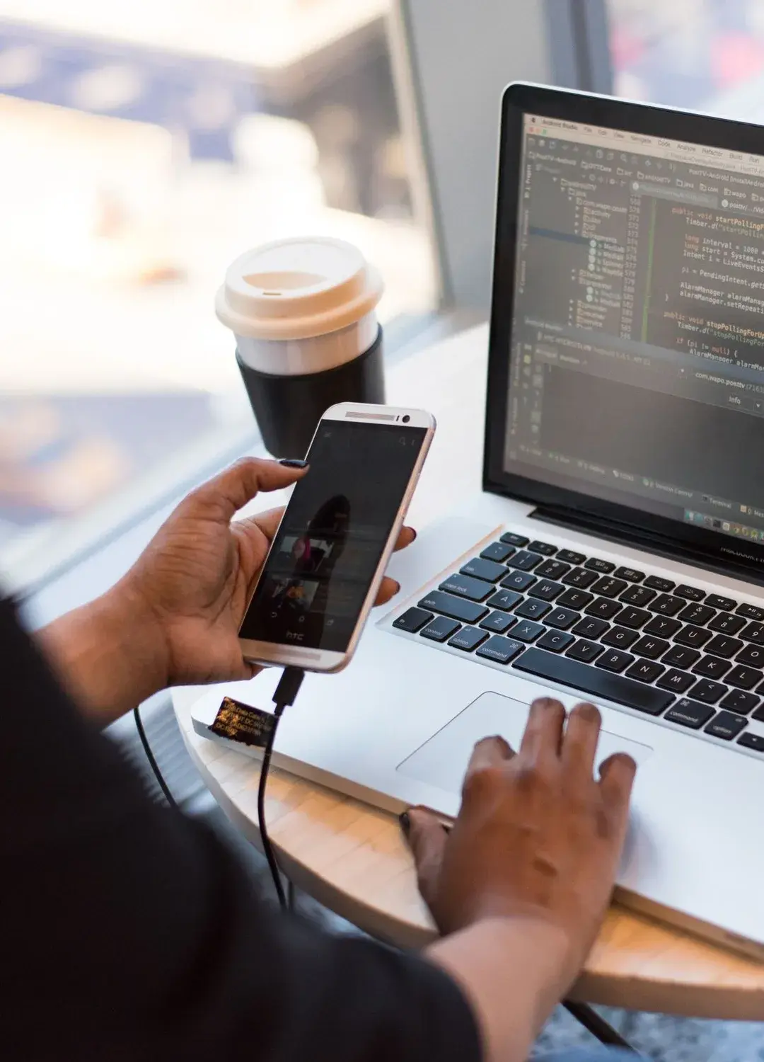 A phone held beside a laptop with code on the screen